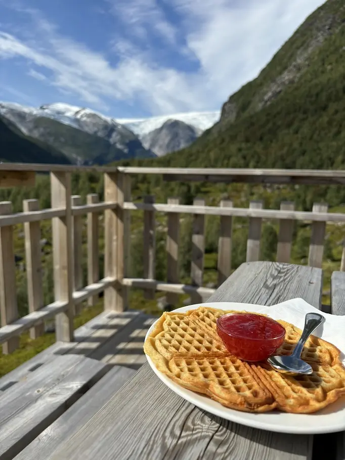 Vanlife Tipps - Essen. Herzwaffel mit Erdbeermarmelade auf Teller. Teller steht auf Holztisch mit Bergen im Hintergrund